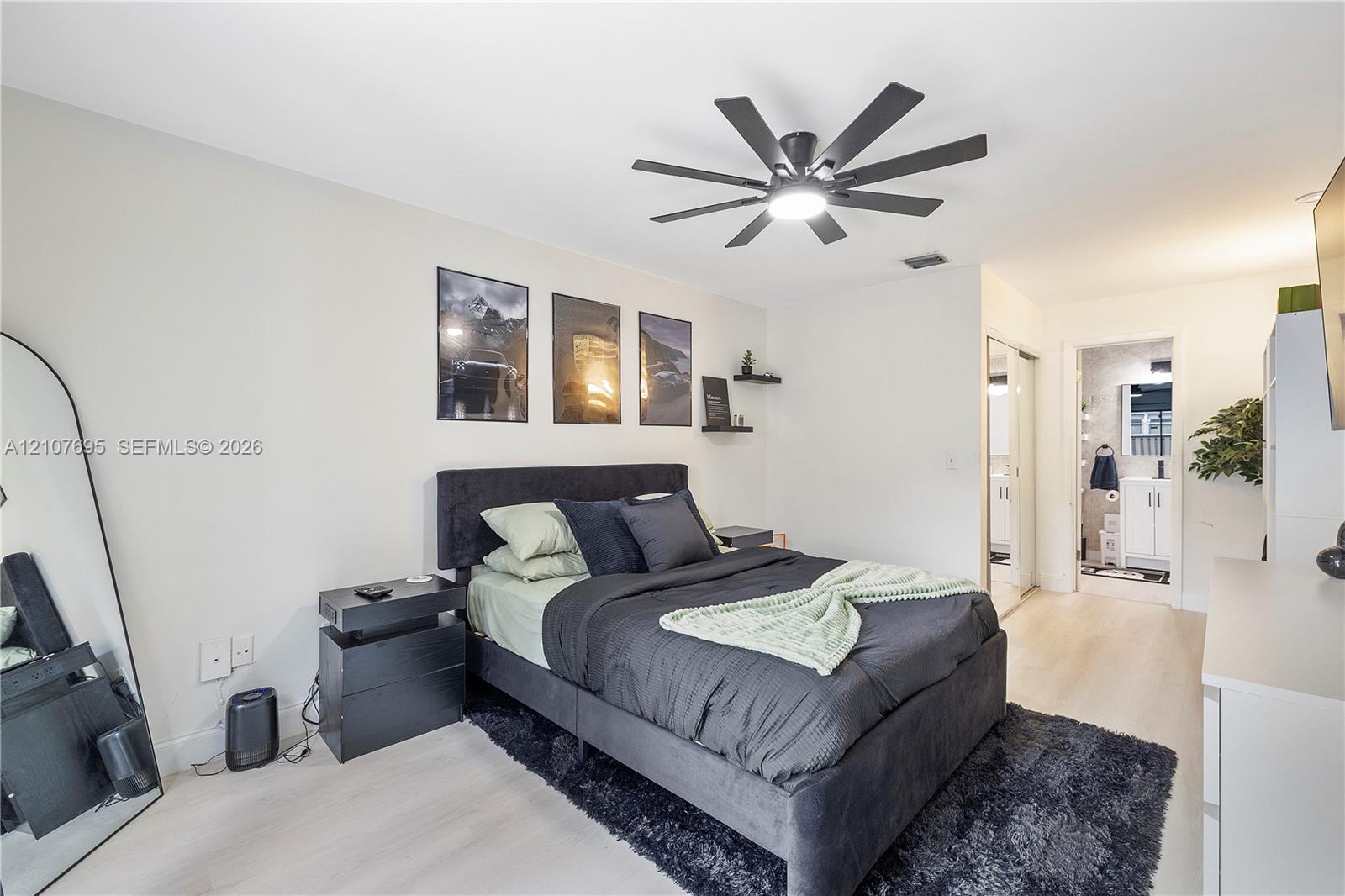 Neutral-toned interior space featuring wood-finish flooring, a multi-blade ceiling fan with integrated lighting, and dual wall-mounted floating shelves