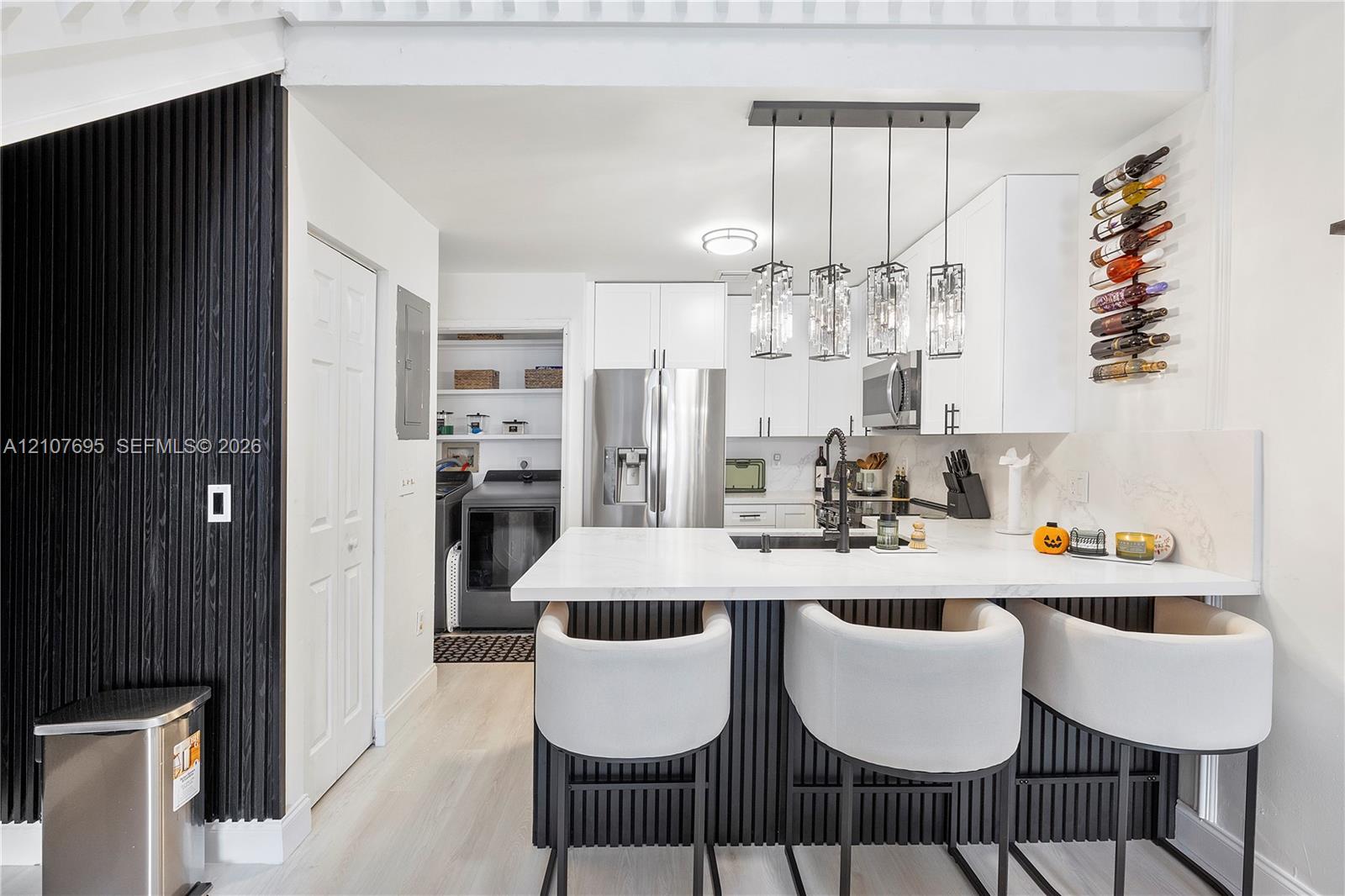 Kitchen featuring white cabinetry, a quartz-topped island with vertical slat detailing, stainless steel appliances, a modern multi-pendant light fixture, and a built-in wall-mounted wine rack