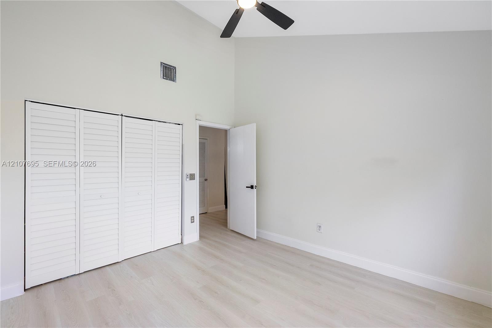 Vaulted ceilings, wood-finish flooring, four-panel louvered closet doors, and a ceiling-mounted light fixture