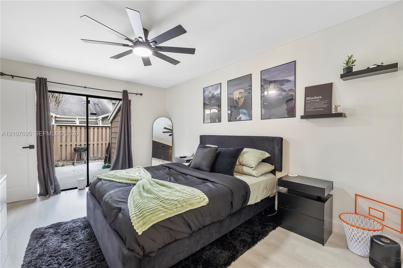 Room featuring light-toned flooring, a multi-blade ceiling fan with integrated lighting, and a sliding glass door providing access to an enclosed patio area
