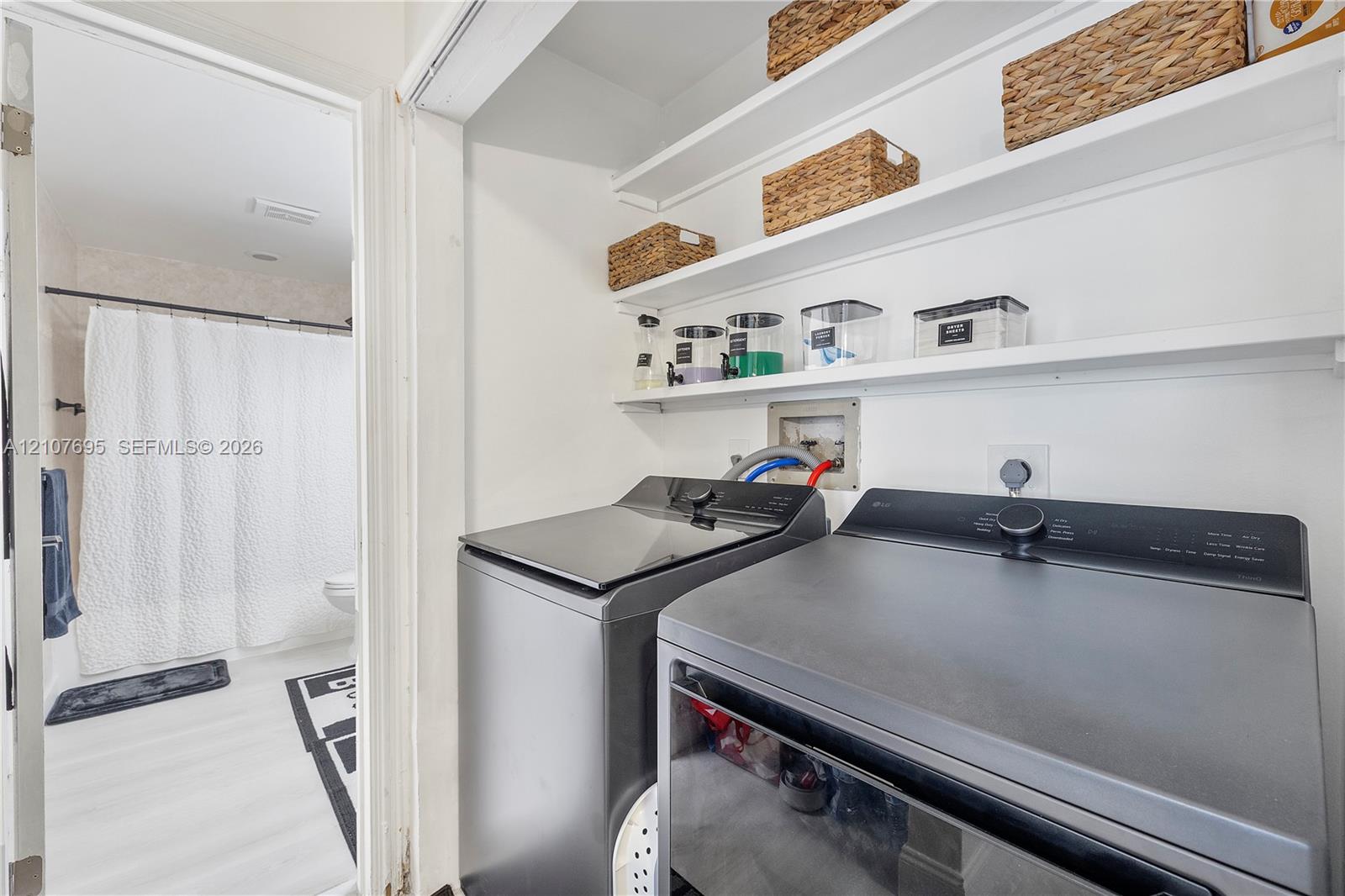 Laundry area featuring built-in shelving, white walls, and wood-finish flooring