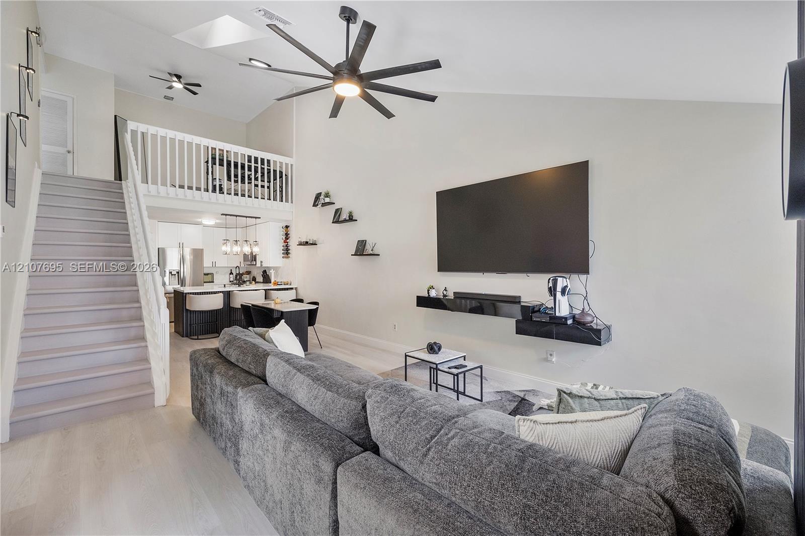 Vaulted ceilings featuring a skylight, multi-blade ceiling fan, and vinyl staircase with white railings