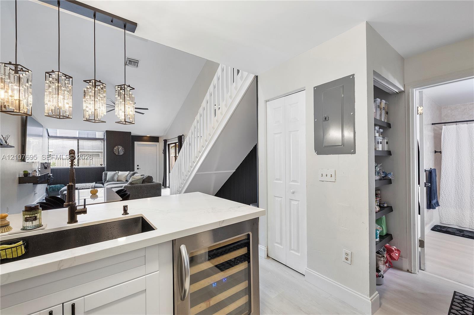 Kitchen featuring a white countertop with an integrated undermount sink, matte black faucet, built-in wine refrigerator, glass pendant lighting, and recessed shelving