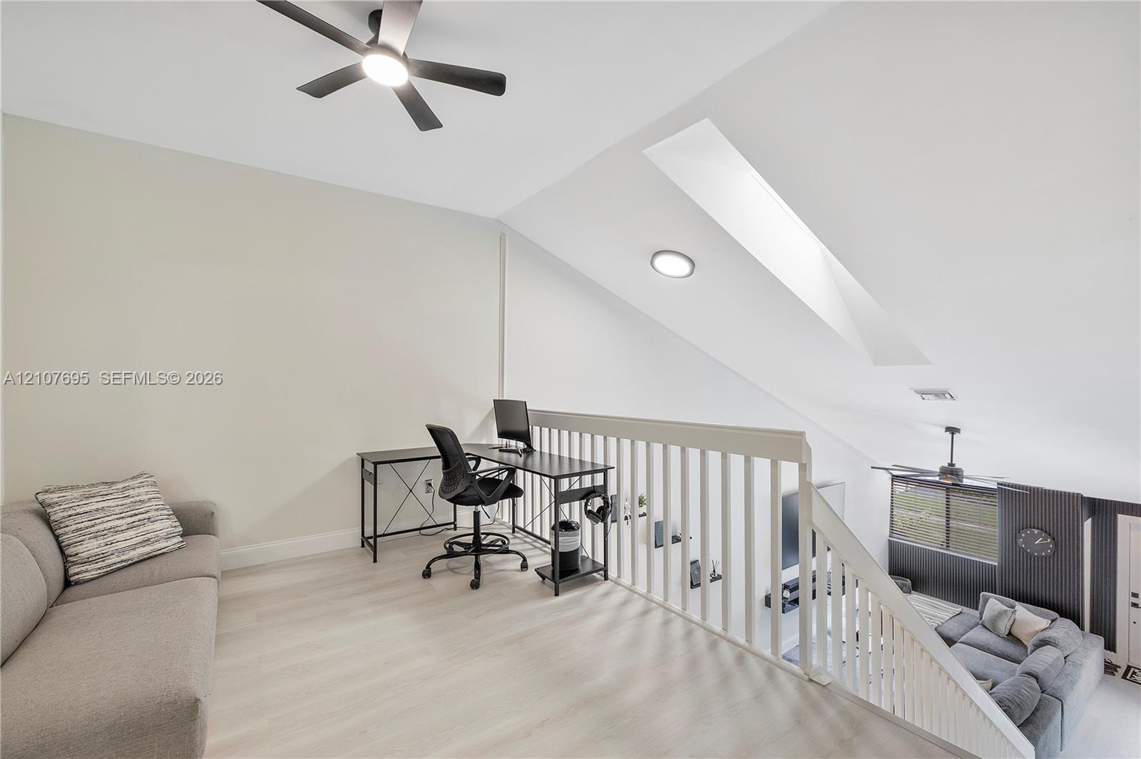 Open loft area featuring vaulted ceilings, a skylight, wood-finish flooring, and a ceiling fan with integrated lighting
