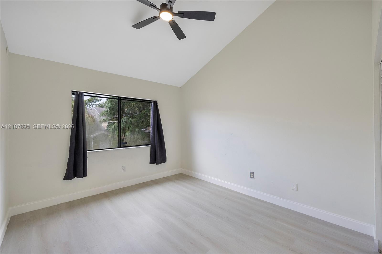 Vaulted ceiling, light-tone wood-finish flooring, and matte black ceiling fan