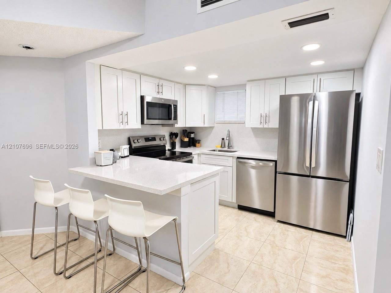 Kitchen featuring white shaker-style cabinetry, quartz countertops, stainless steel appliances, recessed lighting, and tile flooring