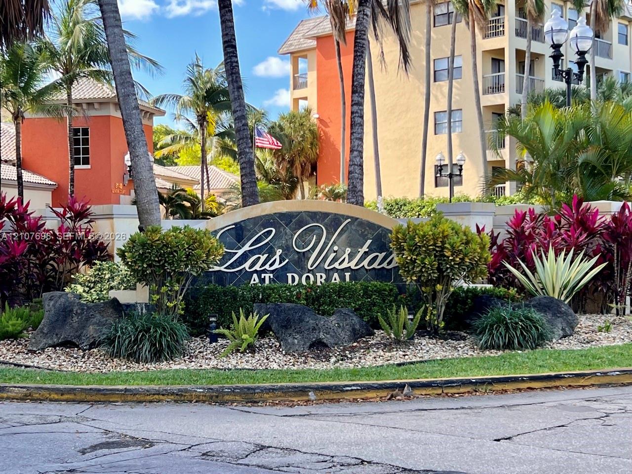 Community entrance monument featuring a stone-inlay sign, mature palm trees, decorative rock accents, and established ornamental landscaping