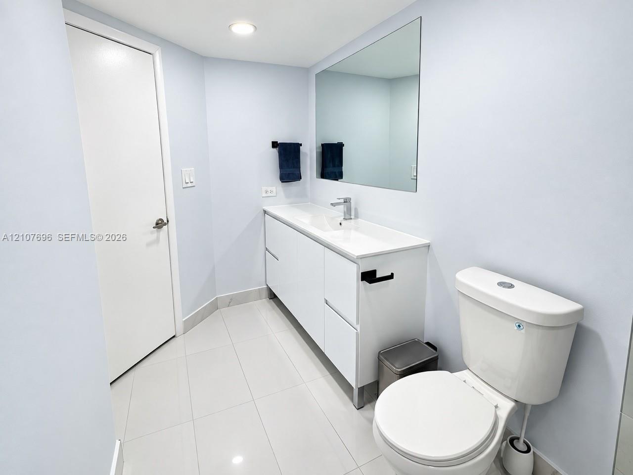 Bathroom featuring white cabinetry, integrated sink, polished tile flooring, large wall-mounted mirror, and matte black fixtures