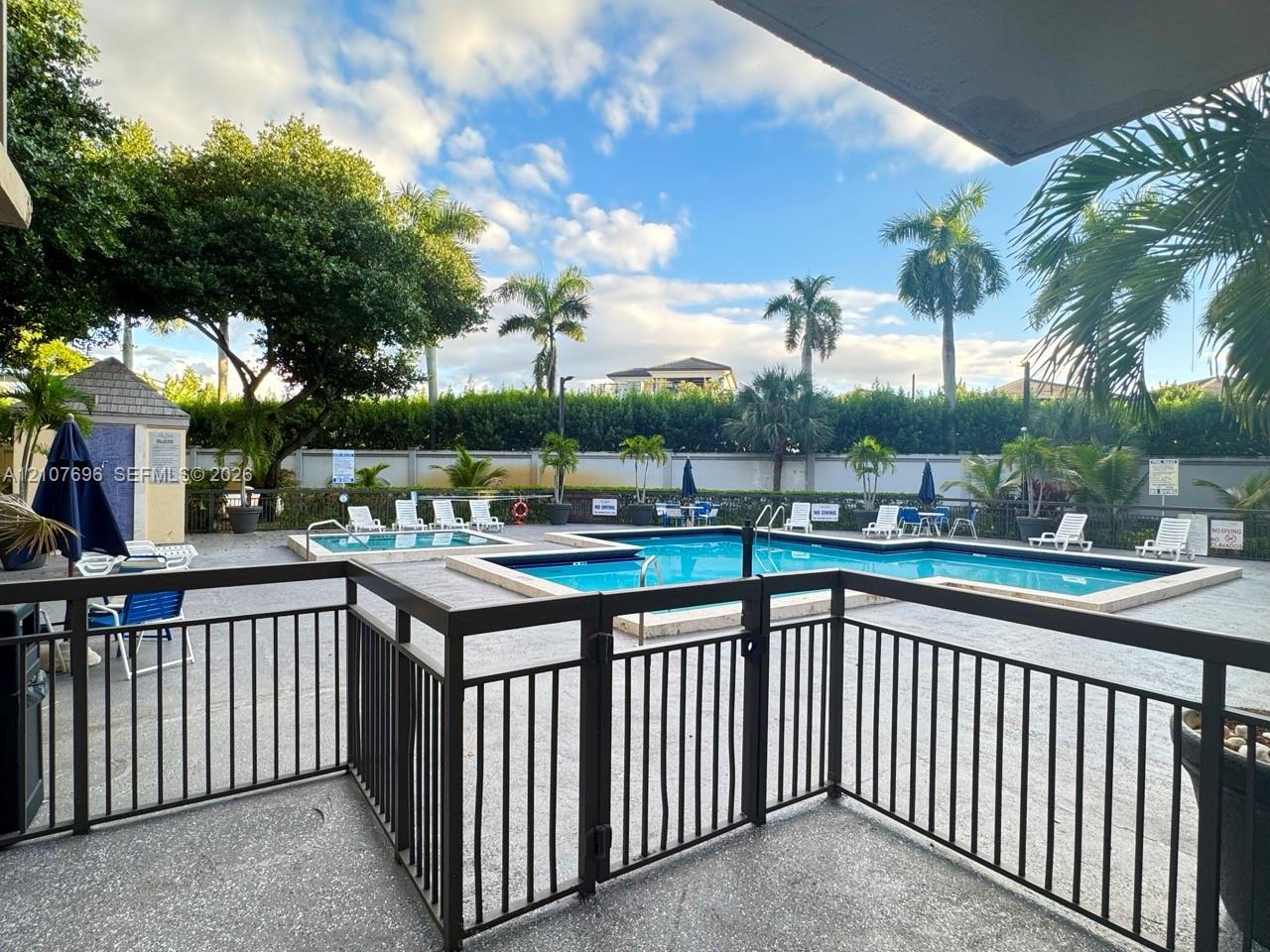 Community pool and spa area featuring a paver deck, metal safety fencing, and established palm trees