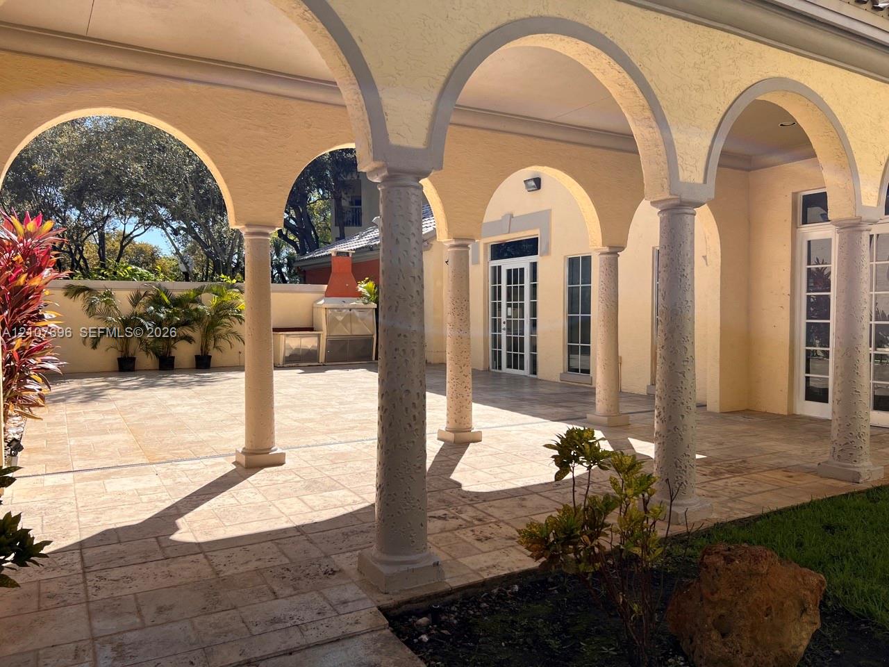 Covered patio featuring structural stone columns, arched masonry detailing, paved flooring, and a built-in outdoor masonry grill