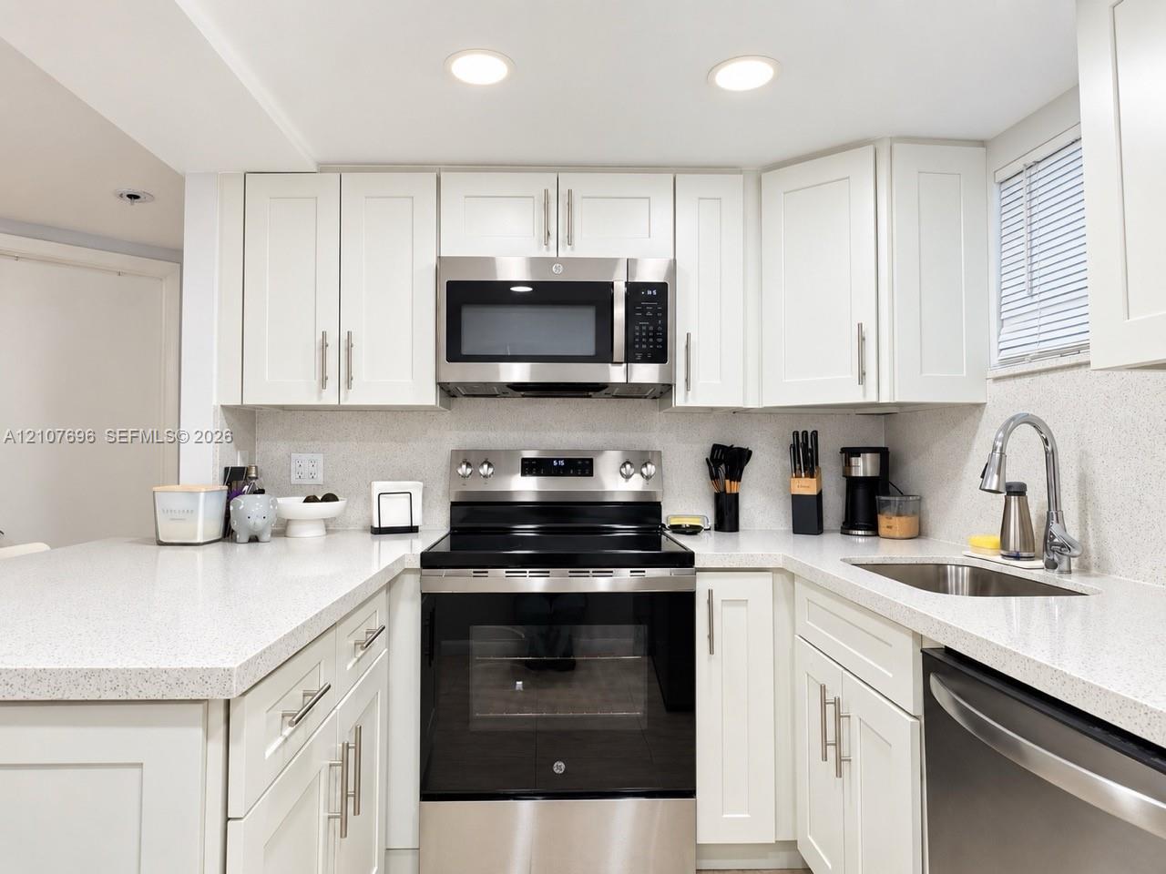 Kitchen featuring shaker-style cabinetry, solid-surface countertops, recessed lighting, and stainless-steel appliances including a range, microwave, and undermount sink