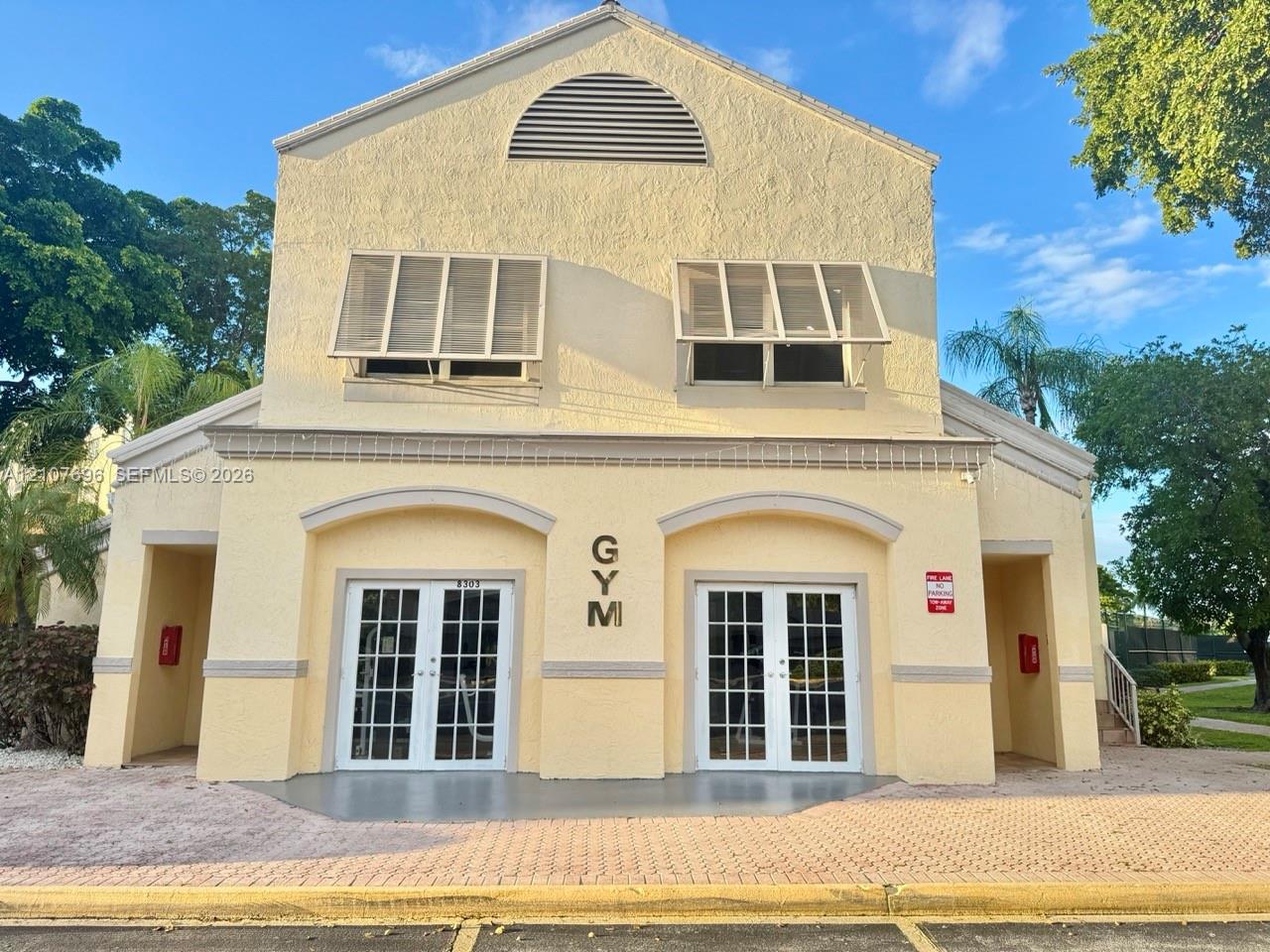 Stucco exterior building featuring arched entryways, dual French doors with glass panes, decorative window shutters, and a semi-circular attic vent