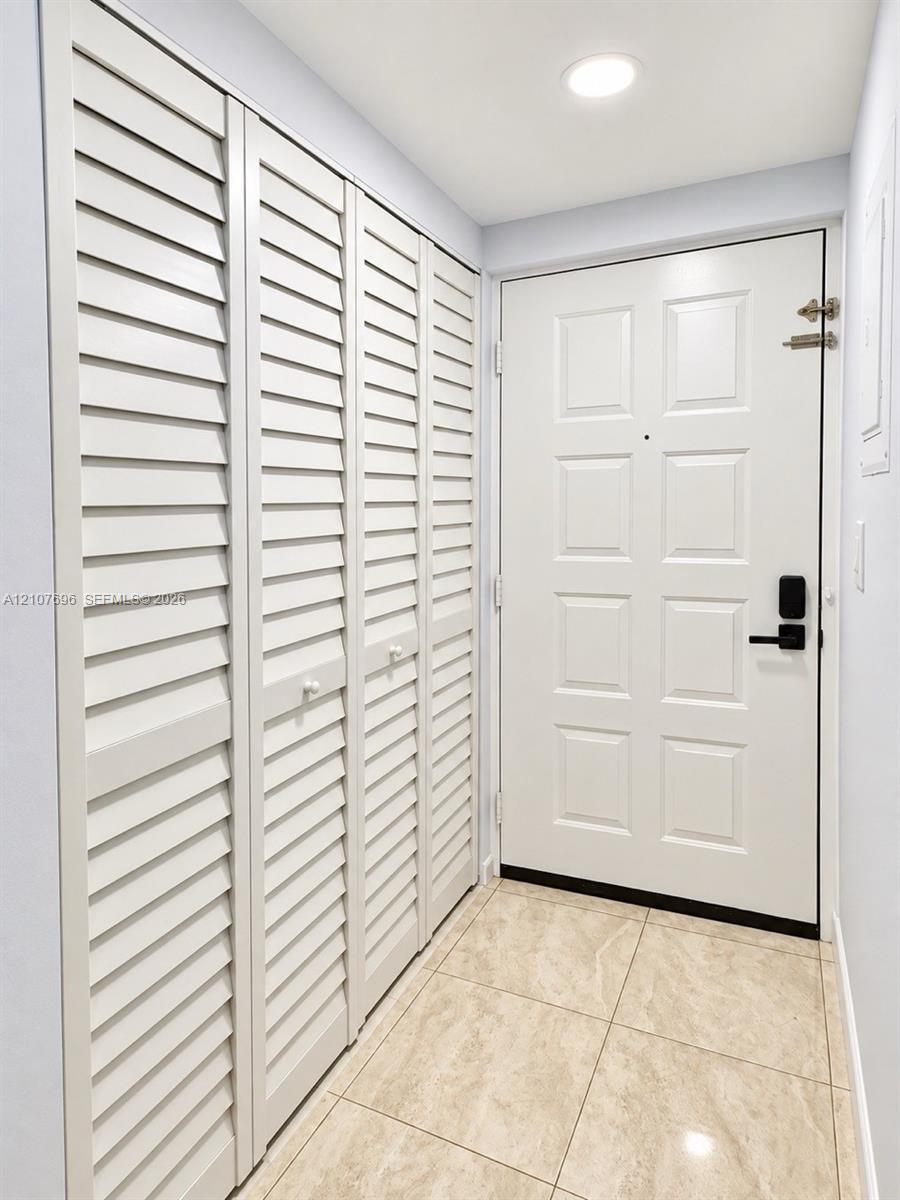 Entryway featuring large-format tile flooring, a six-panel door with matte black hardware, and floor-to-ceiling storage cabinetry with louvered doors