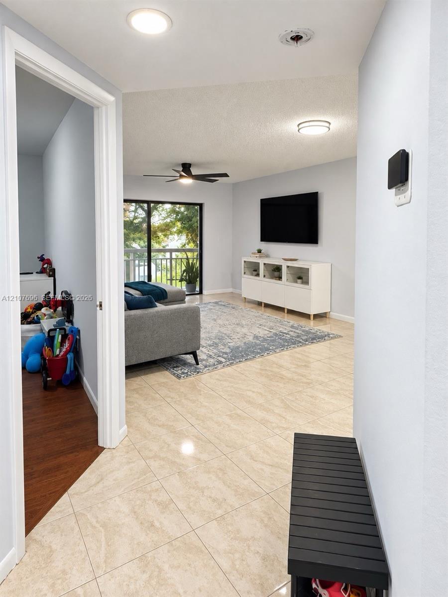 Neutral-tone large-format tile flooring, recessed overhead lighting, matte black ceiling fan, and sliding glass doors with balcony access