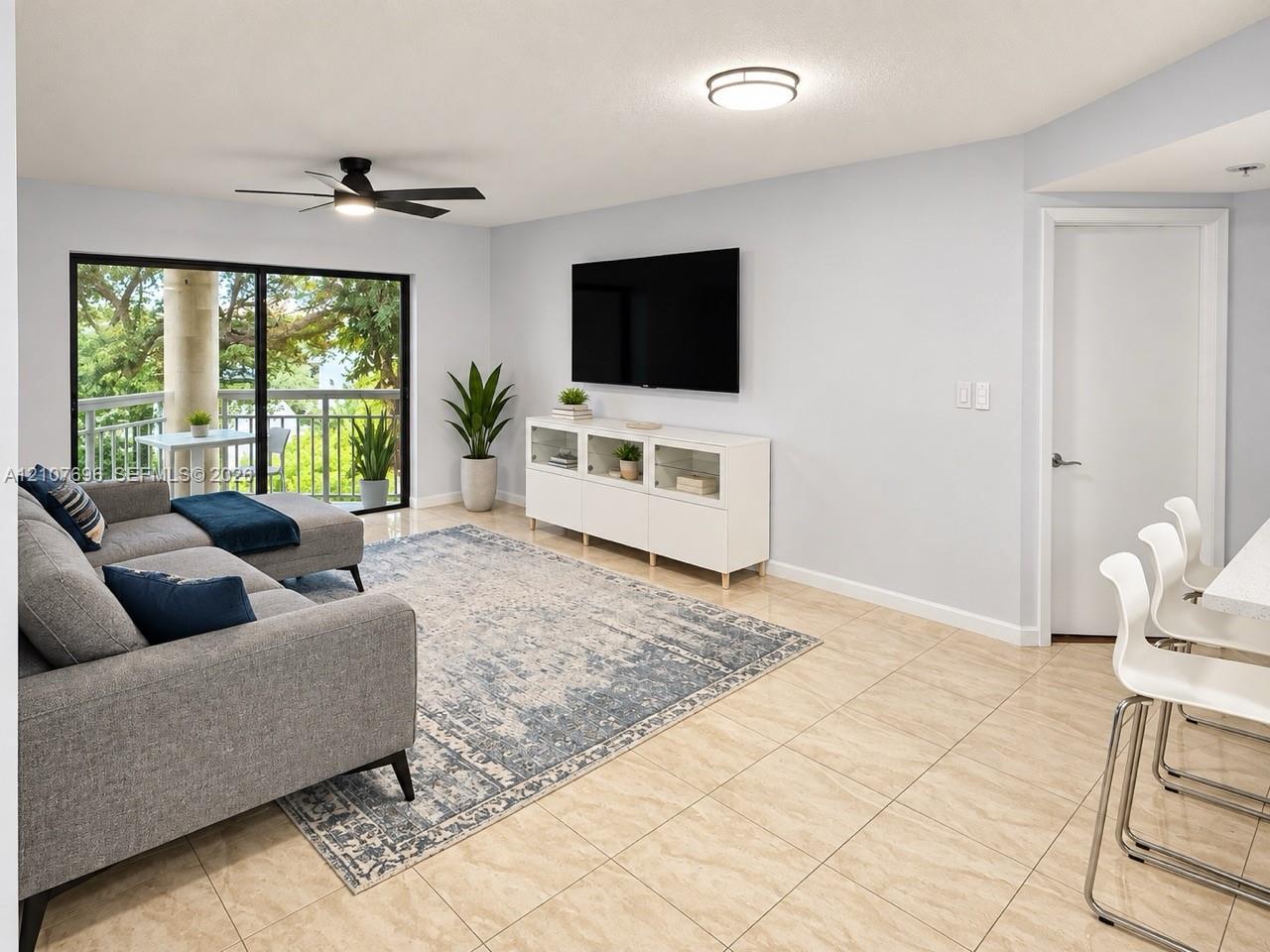 Living area featuring neutral tile flooring, a matte black ceiling fan, and a large sliding glass door providing natural light