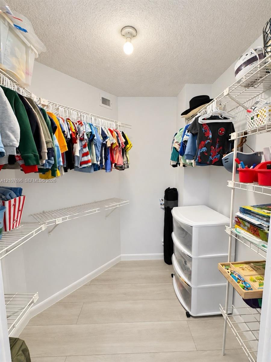 Walk-in closet featuring light-toned wood-finish flooring and multiple levels of integrated wire shelving