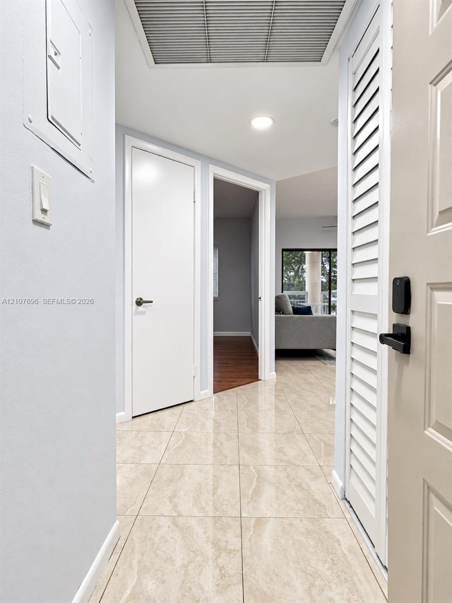 Entryway featuring neutral large-format tile flooring, white six-panel interior doors, and a louvered closet door with matte black hardware