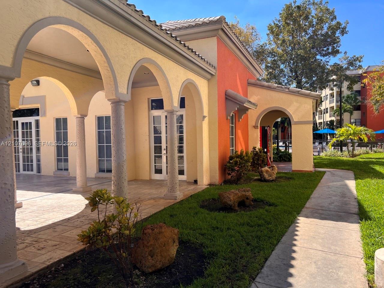 Exterior facade featuring stucco walls, a covered colonnade with arched openings, stone-tile flooring, and glass-paneled double doors