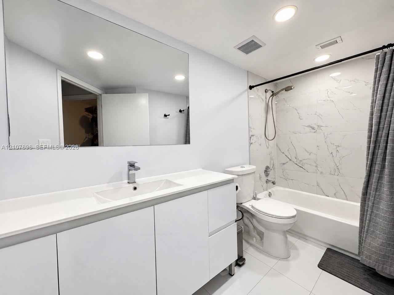 Modern bathroom featuring a high-gloss white vanity with a rectangular sink, large format mirror, stone-finish tile shower surround, and recessed ceiling lighting