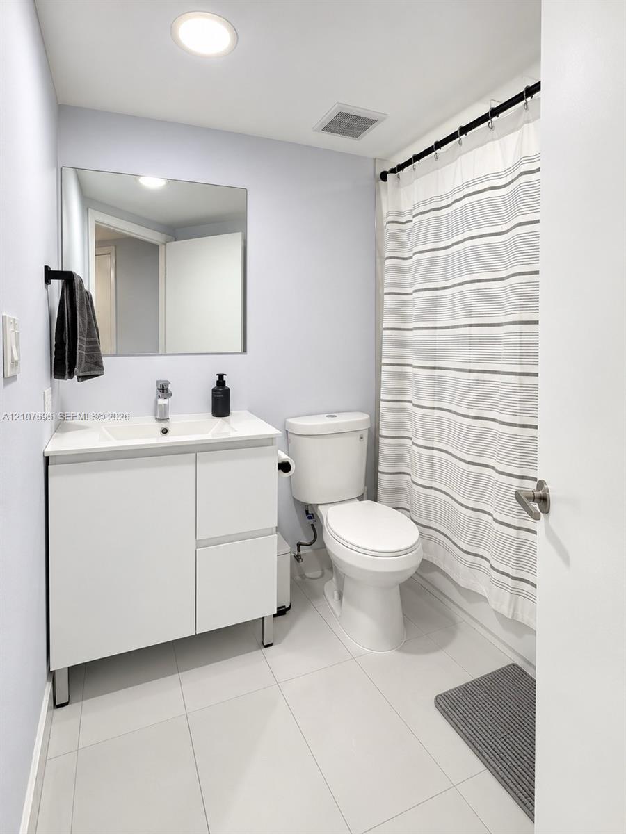 Modern white vanity with a rectangular sink, frameless wall-mounted mirror, polished chrome faucet, and large-format tile flooring