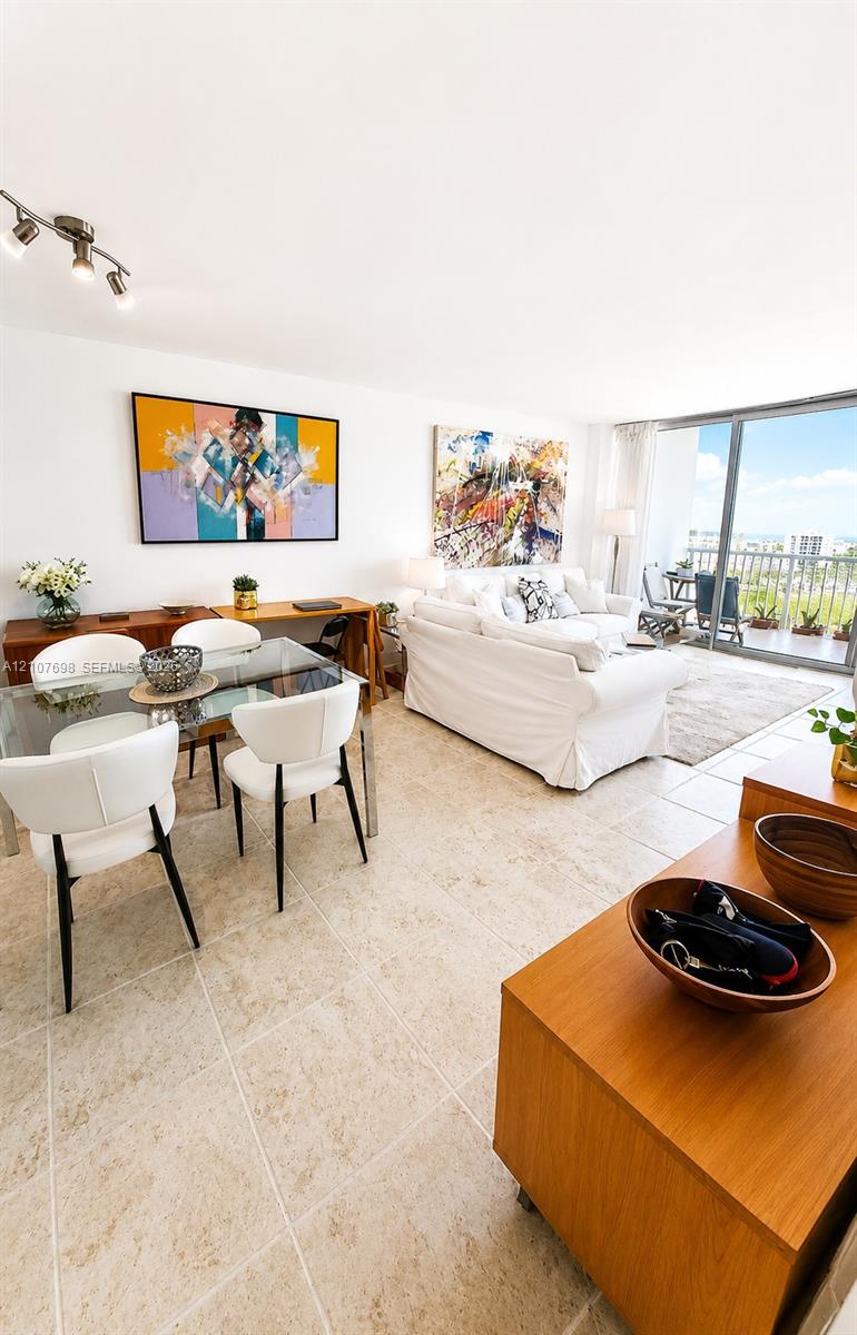Open-concept room featuring light-toned tile flooring, adjustable multi-head track lighting, floor-to-ceiling glass sliding doors, and a private balcony with metal railing