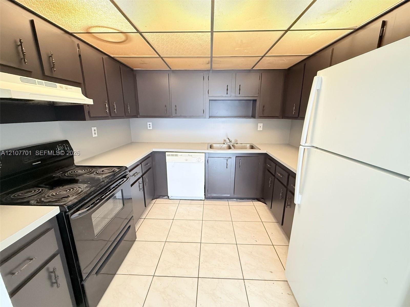 Kitchen featuring dark cabinetry, expansive solid-surface countertops, tile flooring, and integrated dual-basin stainless steel sink