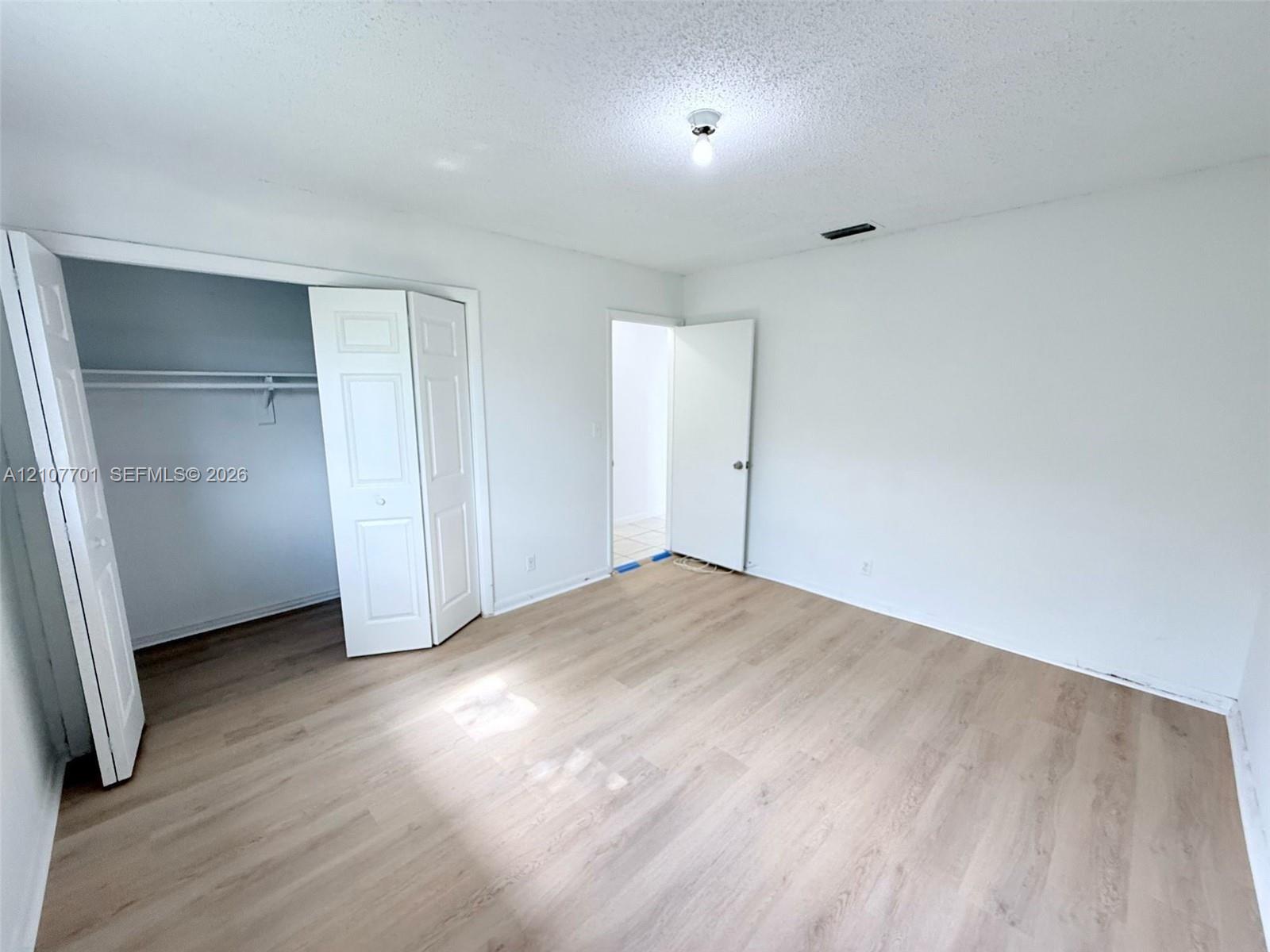 Interior space featuring wood-finish flooring, a built-in reach-in closet with double-panel doors, and a standard swinging door entry Interior space featuring wood-finish flooring, a built-in reach-in closet with double-panel doors, and a standard swinging door entry