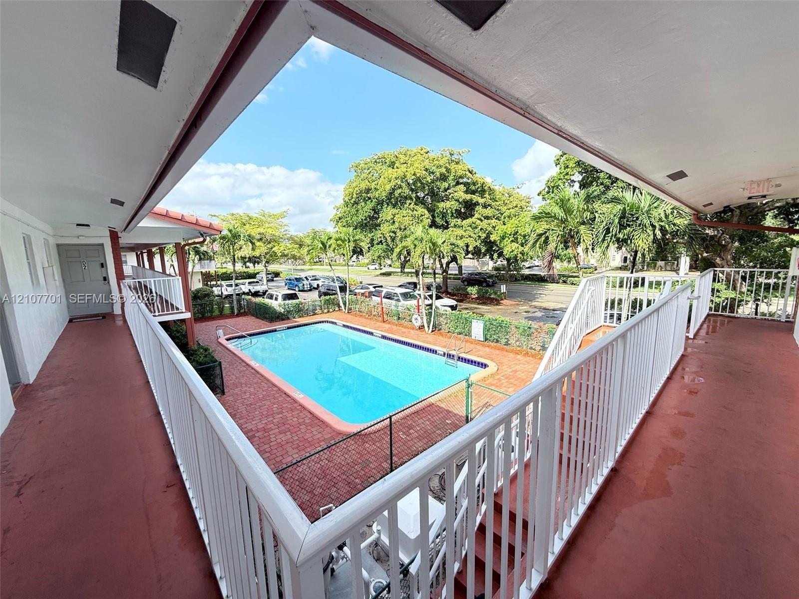Outdoor common area featuring an in-ground swimming pool, brick paver decking, white metal railings, and covered walkway