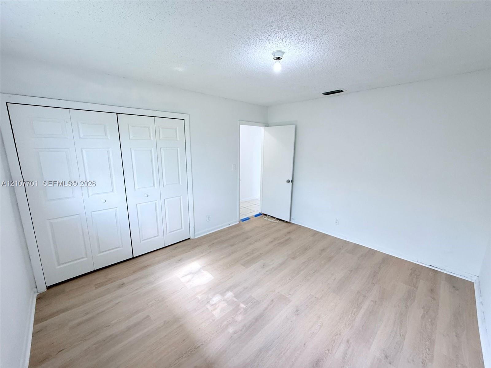 Room featuring wood-finish flooring, dual-panel closet doors, and a ceiling-mounted light fixture