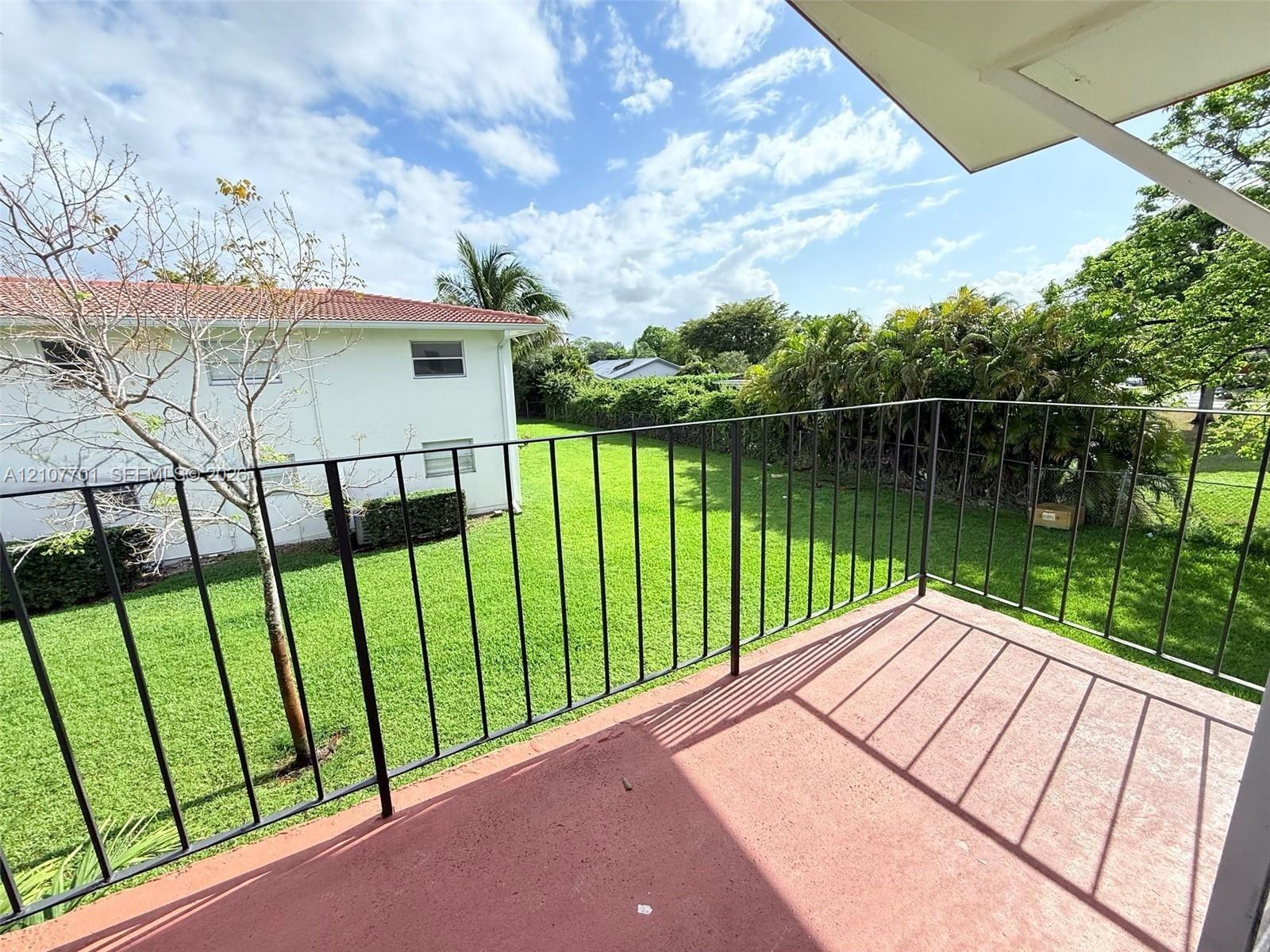 Covered exterior balcony featuring a solid concrete surface and black metal railing, overlooking a large grass lawn