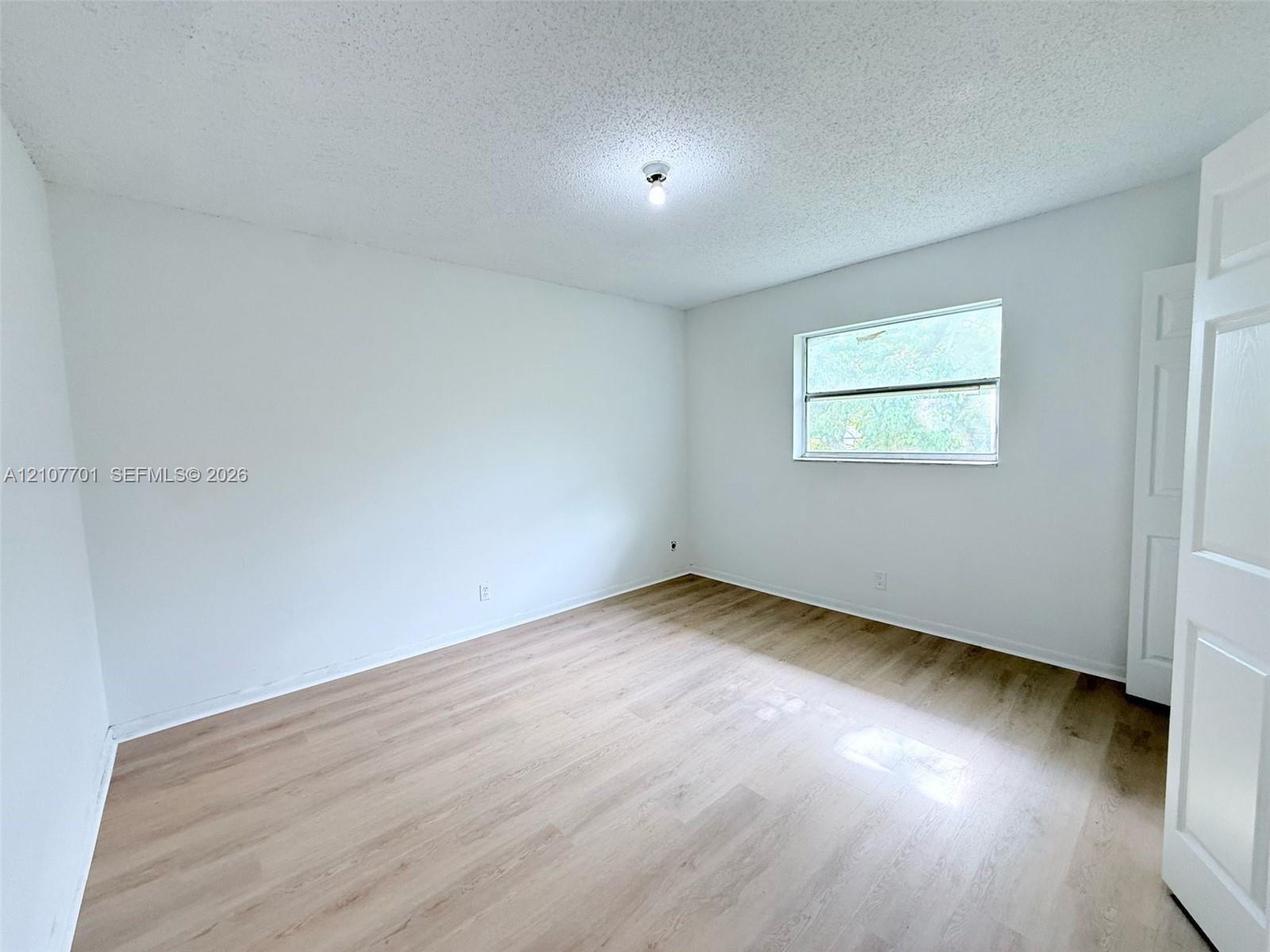 Neutral-toned interior featuring wood-finish flooring, a single horizontal window, and a white multi-panel interior door Neutral-toned interior featuring wood-finish flooring, a single horizontal window, and a white multi-panel interior door