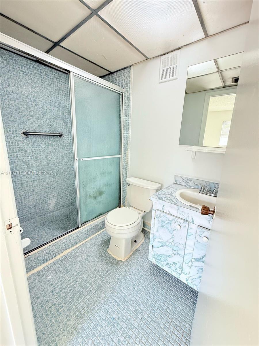 Bathroom featuring a walk-in shower with glass sliding doors, mosaic-tiled flooring and wall surround, a vanity with a patterned stone-finish countertop, and a wall-mounted mirror Bathroom featuring a walk-in shower with glass sliding doors, mosaic-tiled flooring and wall surround, a vanity with a patterned stone-finish countertop, and a wall-mounted mirror