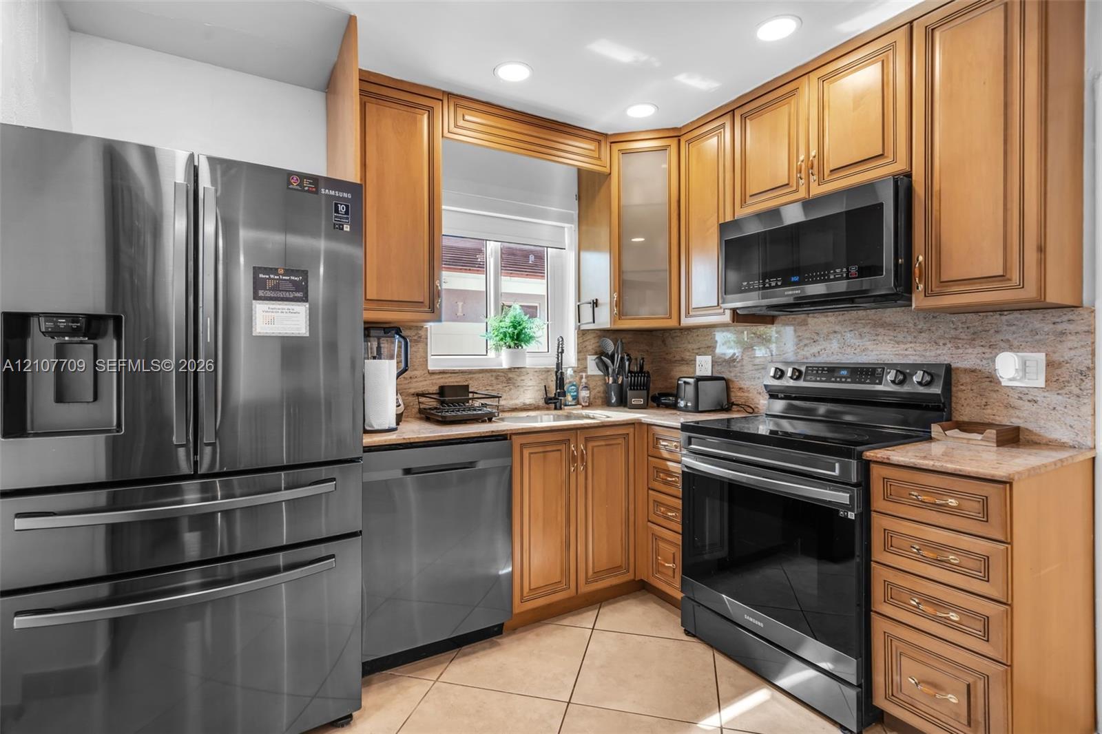 Kitchen featuring wood cabinetry, stone countertops, stainless steel appliances, recessed ceiling lighting, and tile flooring