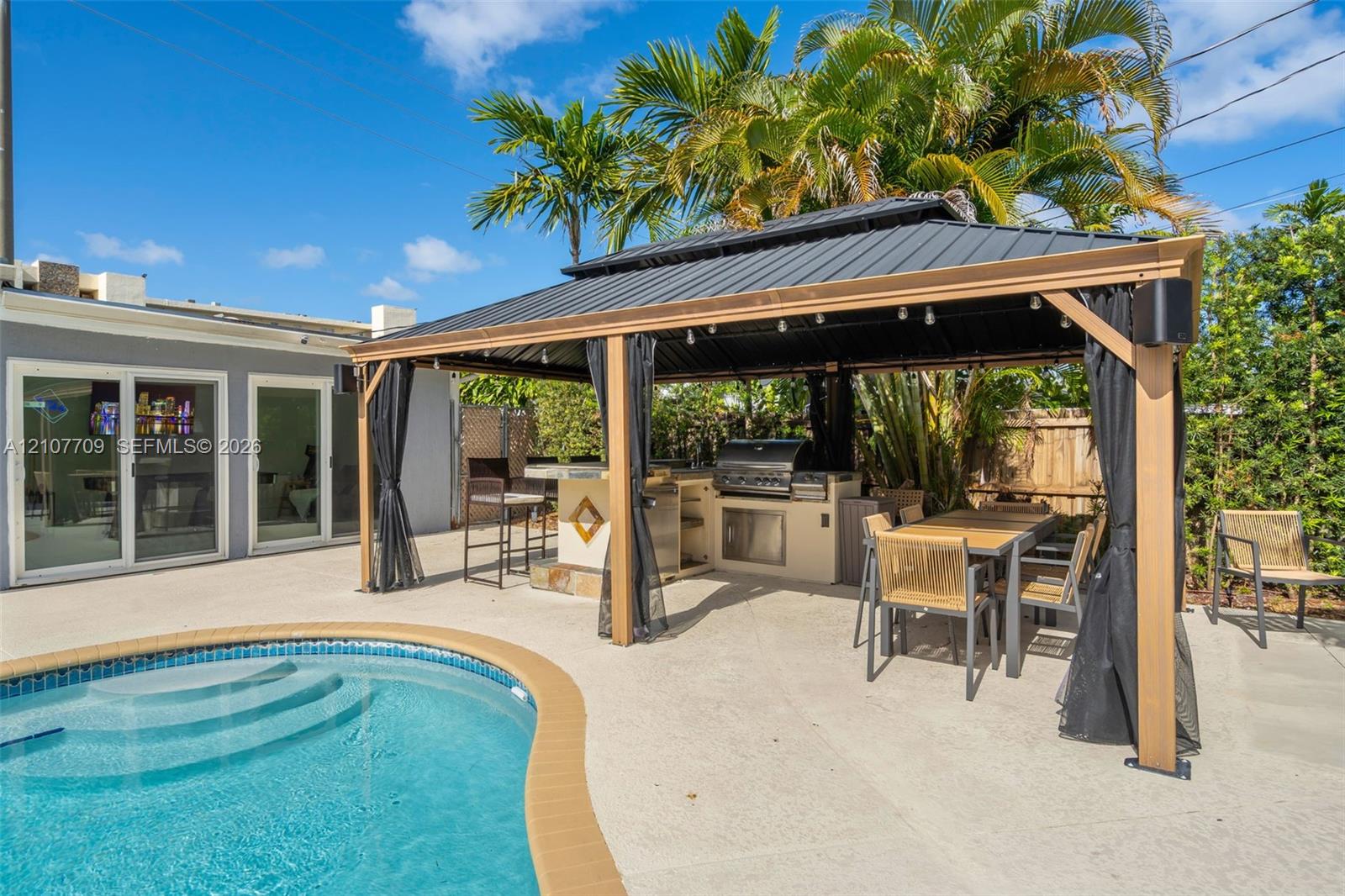 Outdoor living area featuring a covered gazebo, built-in stainless steel grill, concrete patio, and in-ground swimming pool