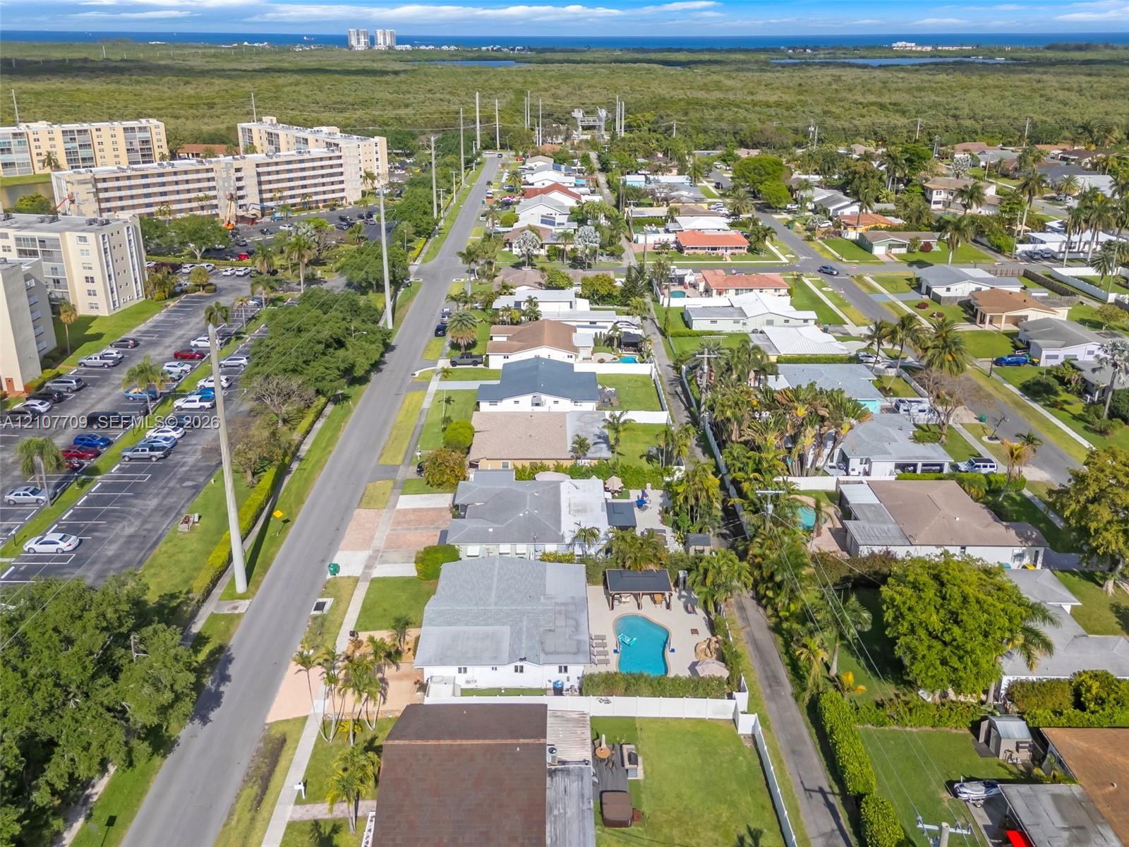Aerial perspective featuring a private swimming pool, concrete patio, mature landscaping, and coastal horizon