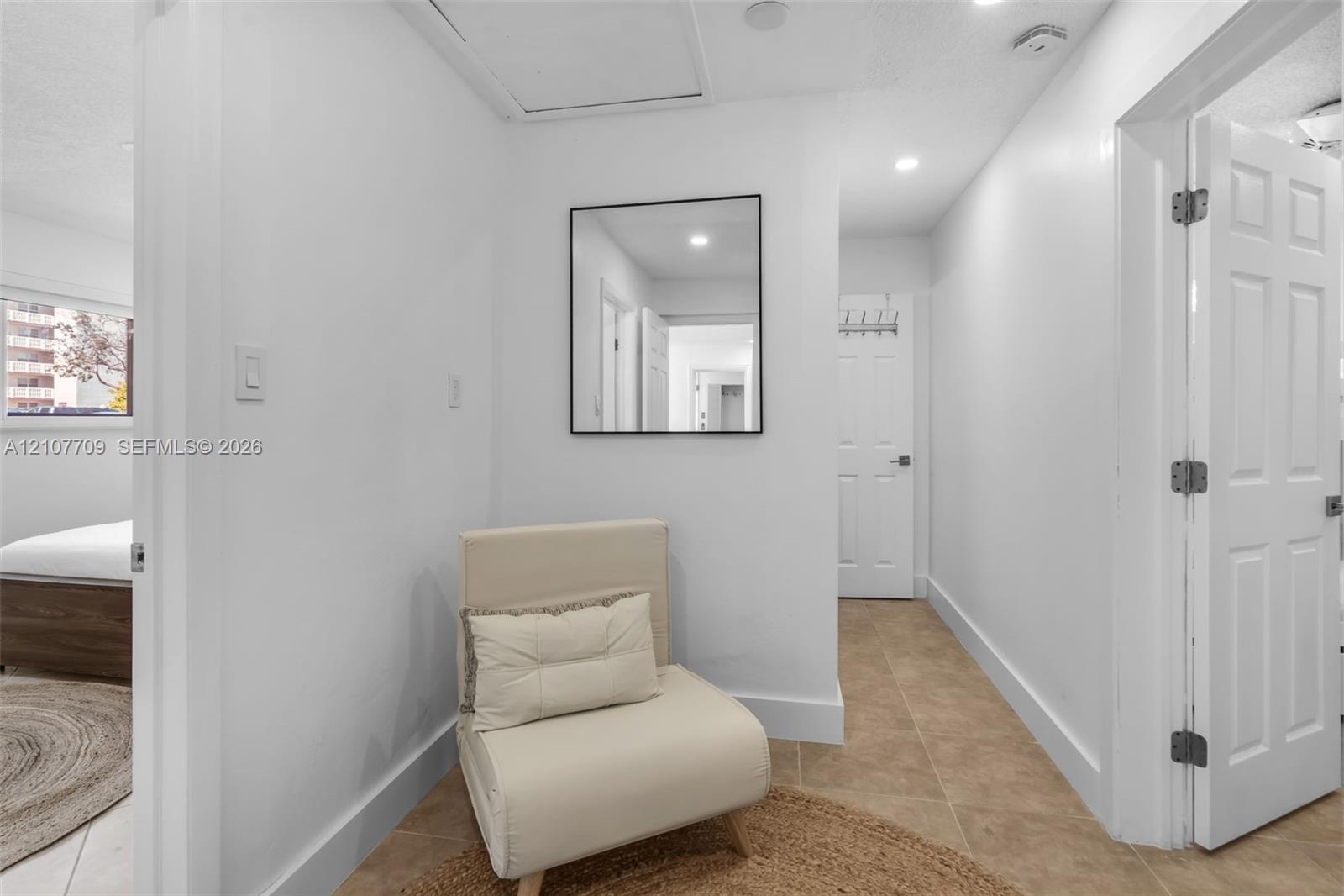 Neutral tile flooring, recessed lighting, and wall-mounted square mirror with a black frame