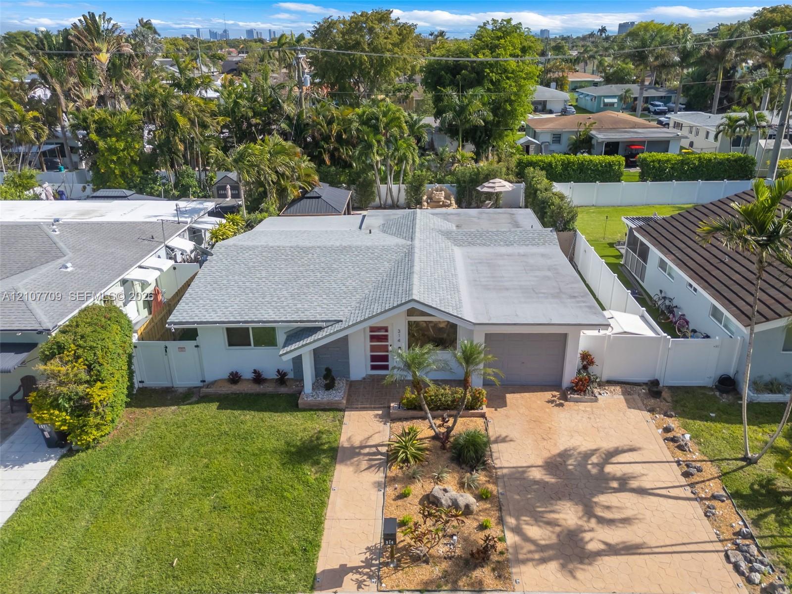 Single-story residence featuring a shingled roof, paver driveway, white privacy fencing, manicured lawn, and professional xeriscape landscaping