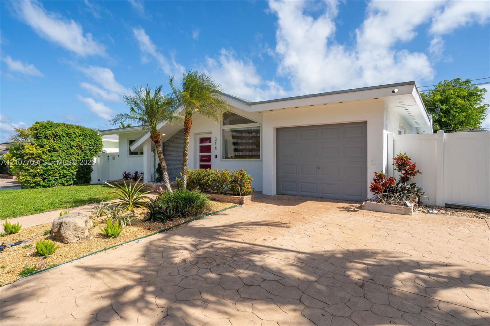 Single-story exterior featuring a stamped concrete driveway, one-car garage, high-pitched roofline with a triangular window, and professional landscaping