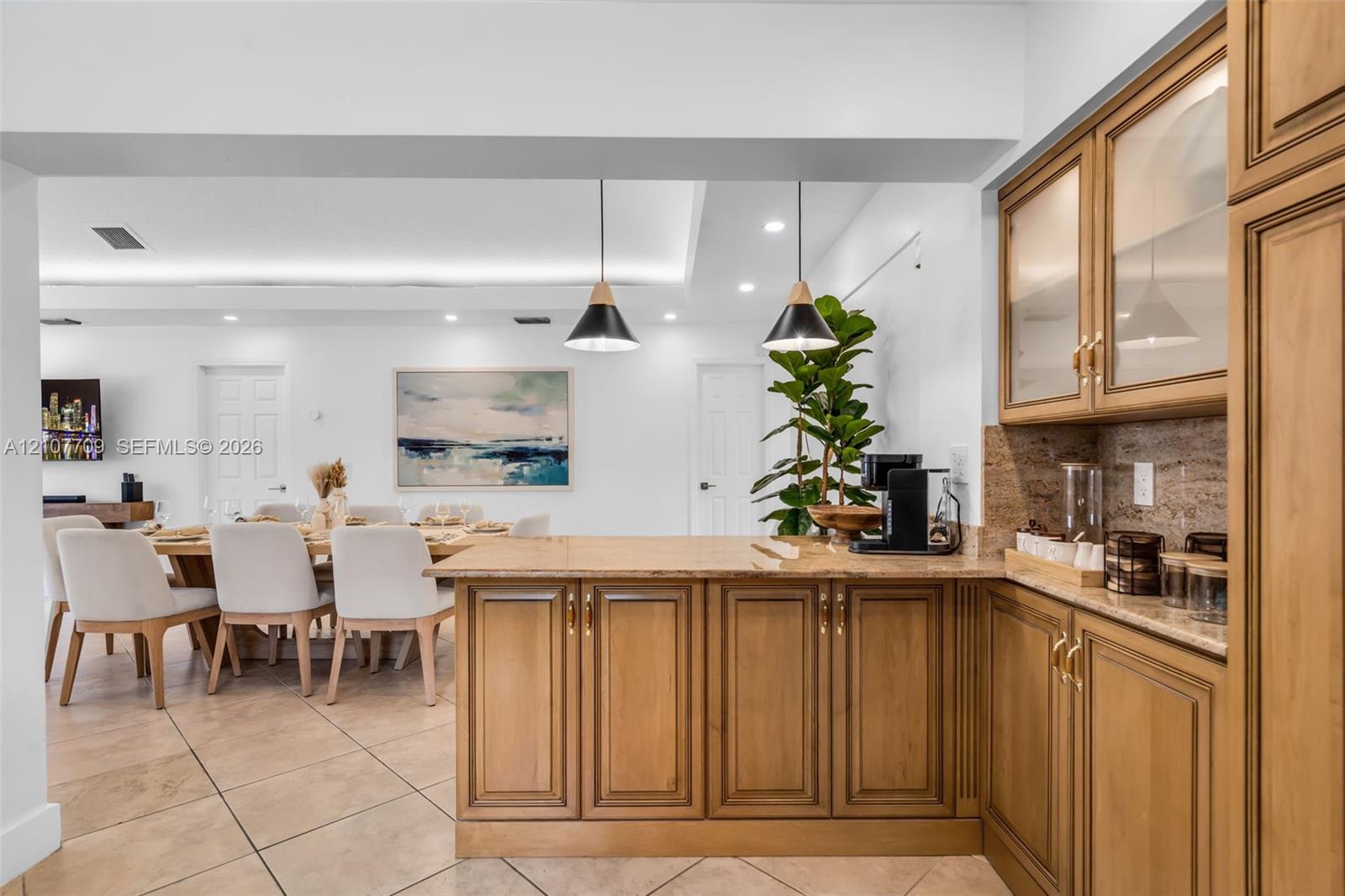Custom cabinetry featuring glass-front upper doors, stone-finish countertops, tile flooring, and dual pendant lighting