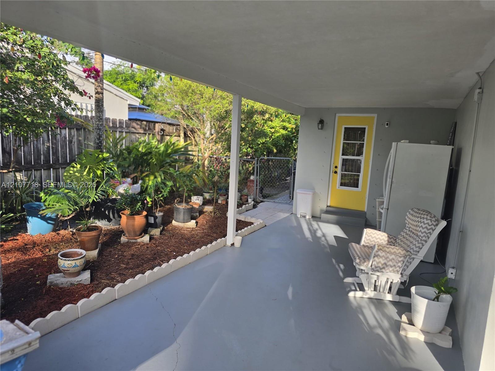 Covered concrete patio featuring a scalloped concrete landscape border, wood-mulch garden bed, and a exterior door with a multi-pane glass insert Covered concrete patio featuring a scalloped concrete landscape border, wood-mulch garden bed, and a exterior door with a multi-pane glass insert