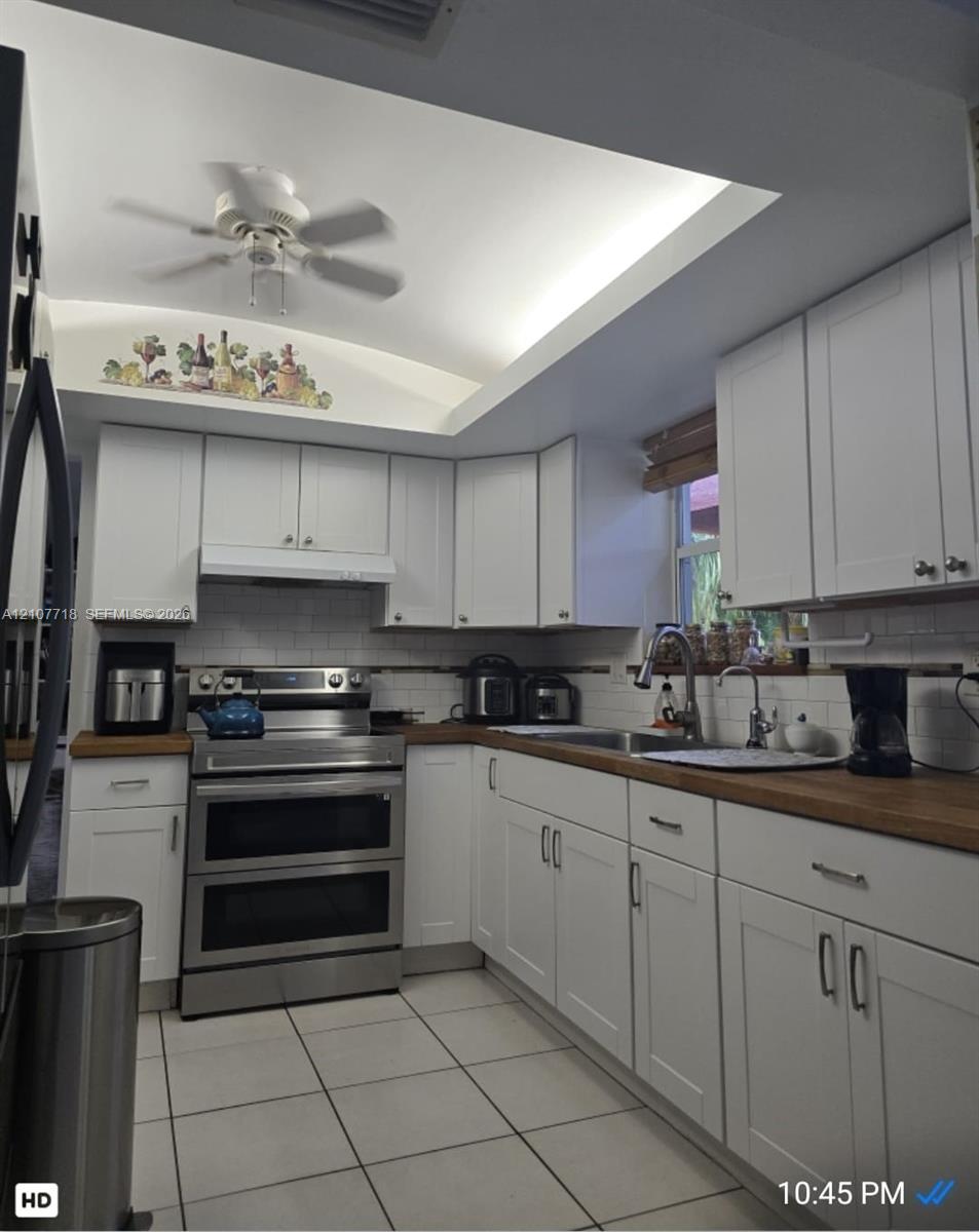 White cabinetry with shaker-style doors, wood-finish countertops, stainless steel dual-oven range, subway tile backsplash, and recessed tray ceiling with integrated lighting White cabinetry with shaker-style doors, wood-finish countertops, stainless steel dual-oven range, subway tile backsplash, and recessed tray ceiling with integrated lighting