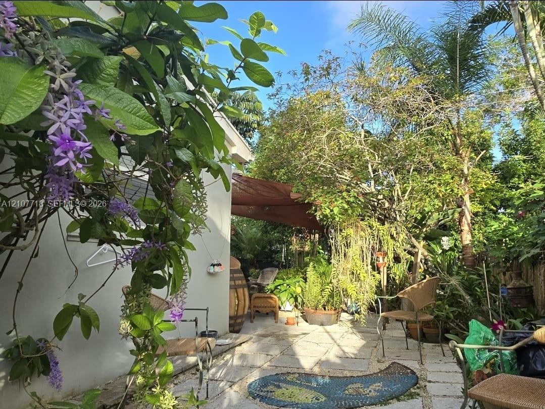 Landscaped outdoor area featuring stone paver flooring, established trees, flowering vines, and a textile shade canopy Landscaped outdoor area featuring stone paver flooring, established trees, flowering vines, and a textile shade canopy