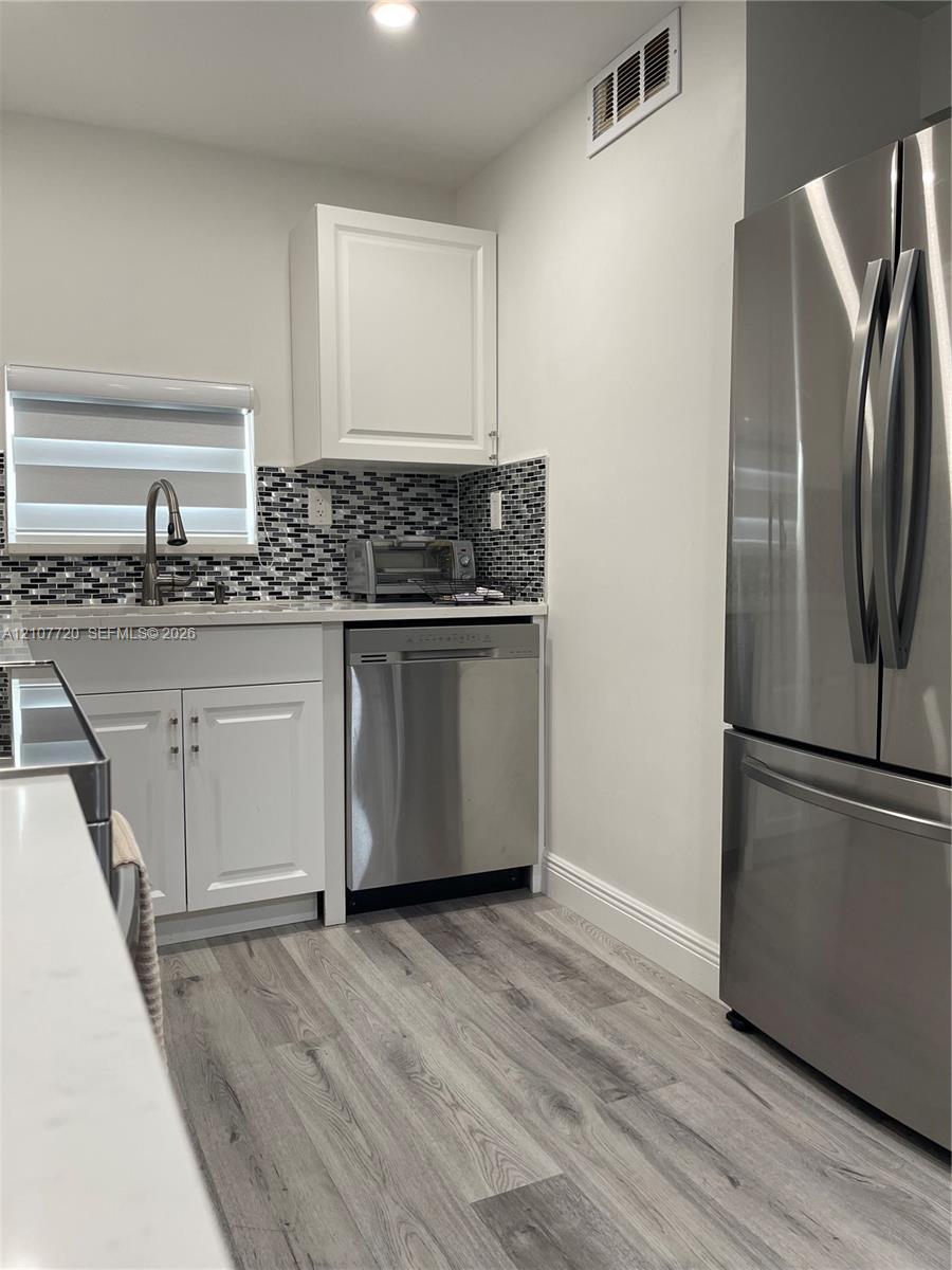 Kitchen featuring white shaker-style cabinetry, wood-finish flooring, stainless steel appliances, and a mosaic tile backsplash Kitchen featuring white shaker-style cabinetry, wood-finish flooring, stainless steel appliances, and a mosaic tile backsplash
