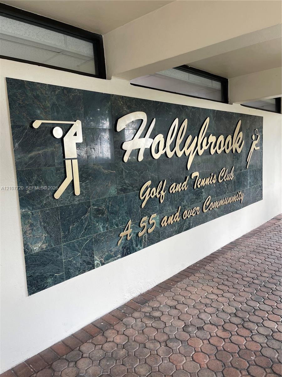 Stone-tiled signage featuring metallic lettering and integrated golf and tennis iconography, set against a paved brick walkway