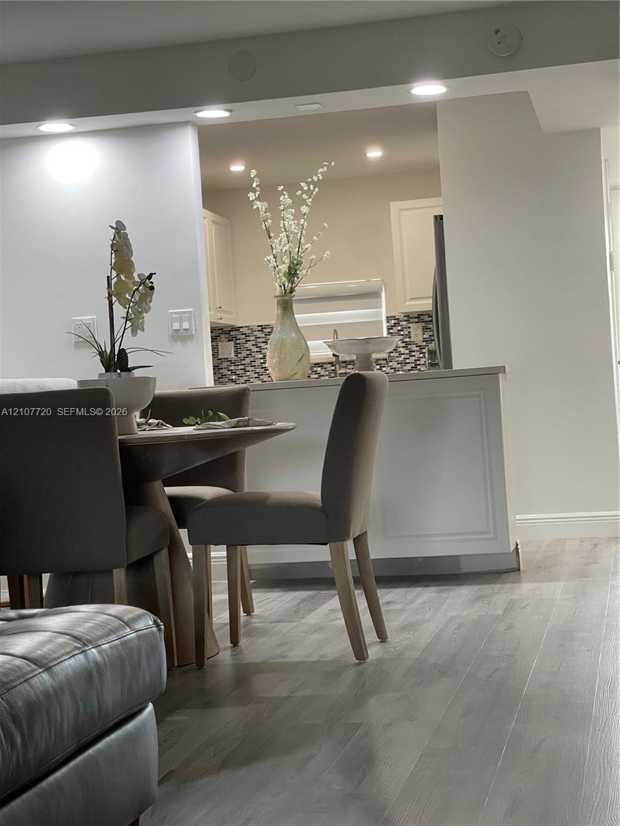 Kitchen featuring a peninsula with paneled cabinetry, mosaic tile backsplash, wood-finish flooring, and recessed ceiling lighting Kitchen featuring a peninsula with paneled cabinetry, mosaic tile backsplash, wood-finish flooring, and recessed ceiling lighting
