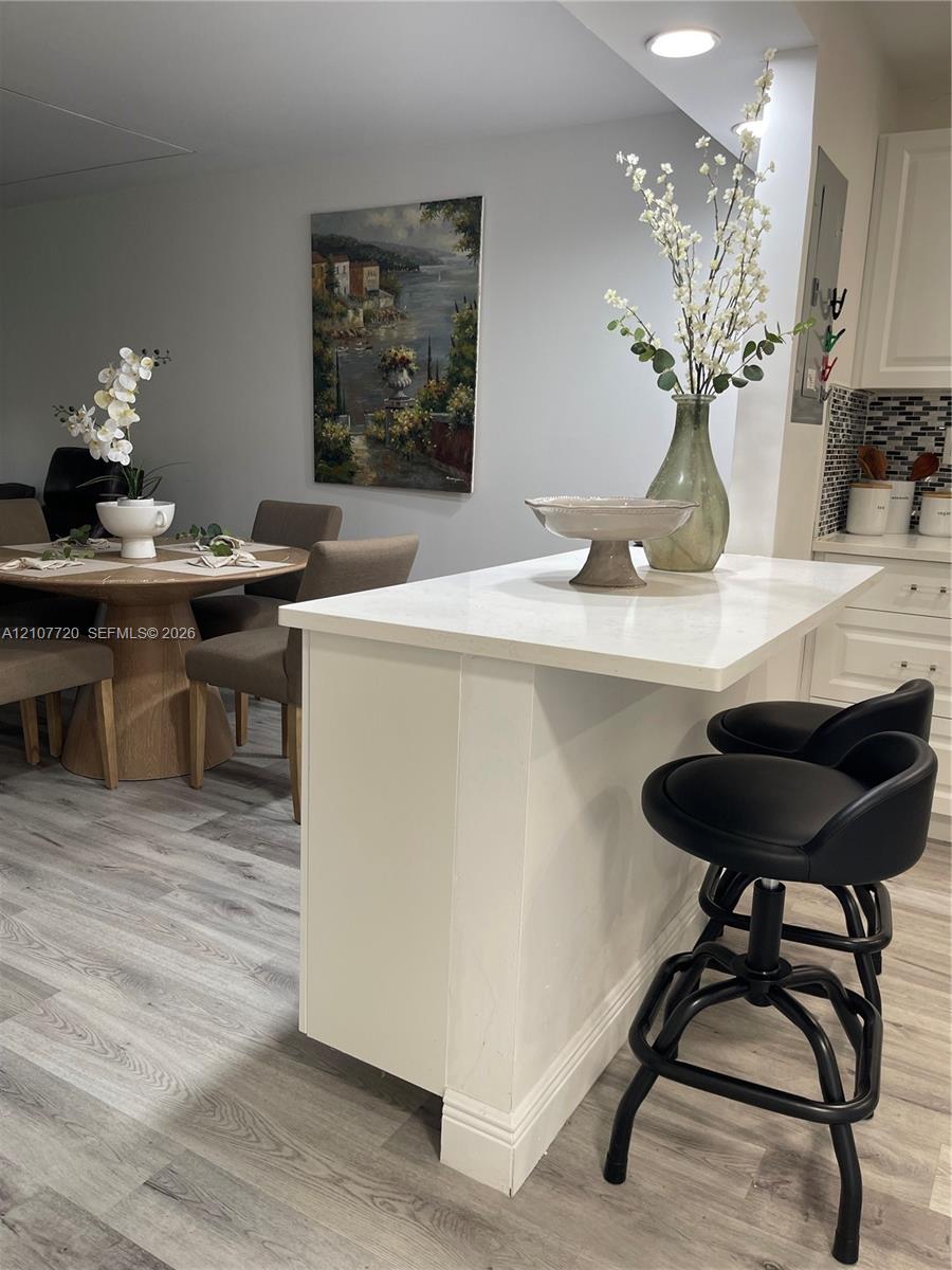 Kitchen peninsula featuring a white countertop and white cabinetry, complemented by wood-finish flooring and a multi-toned mosaic tile backsplash Kitchen peninsula featuring a white countertop and white cabinetry, complemented by wood-finish flooring and a multi-toned mosaic tile backsplash