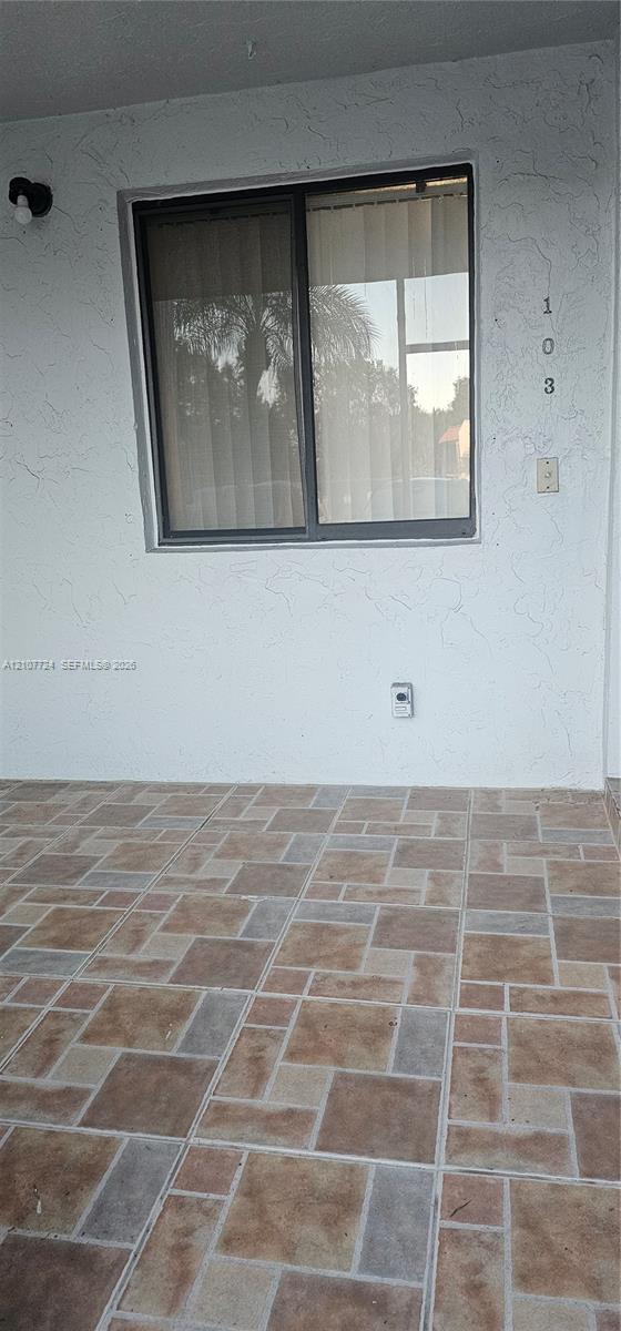 Covered exterior entryway featuring textured white stucco walls, multi-tonal decorative tile flooring, and a single-pane sliding window Covered exterior entryway featuring textured white stucco walls, multi-tonal decorative tile flooring, and a single-pane sliding window