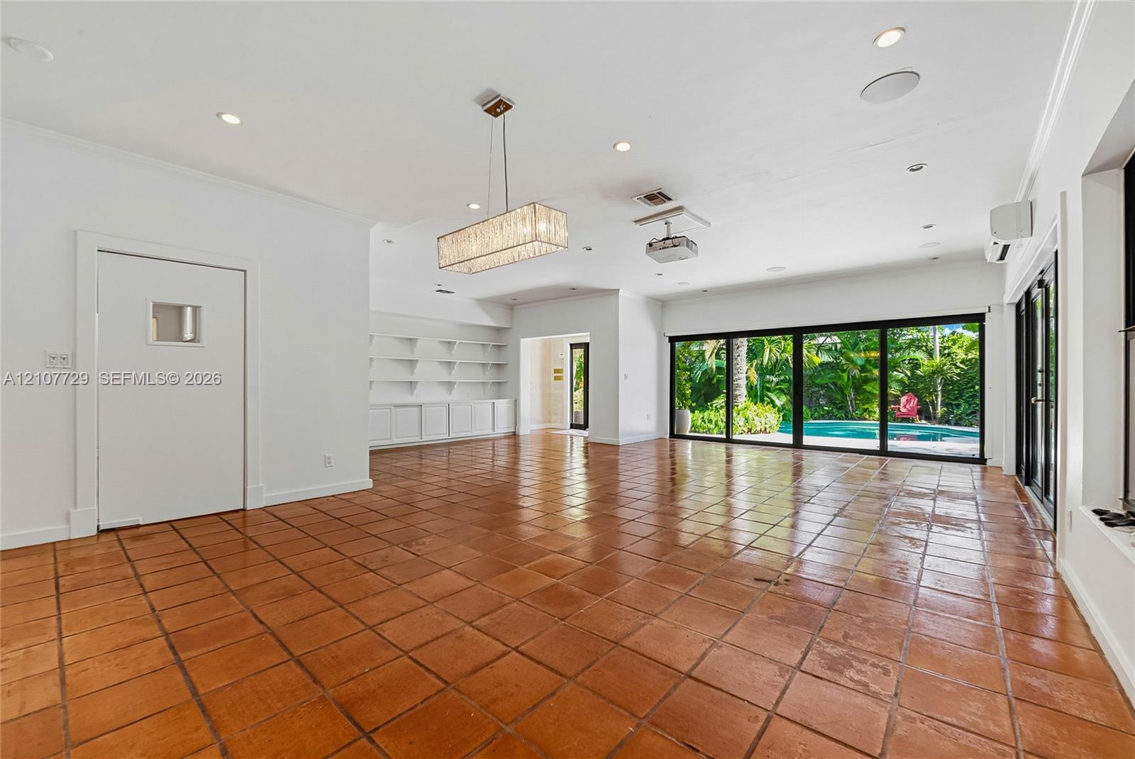 Tile flooring, multi-panel sliding glass doors, built-in shelving, rectangular crystal-style chandelier, and recessed ceiling lighting