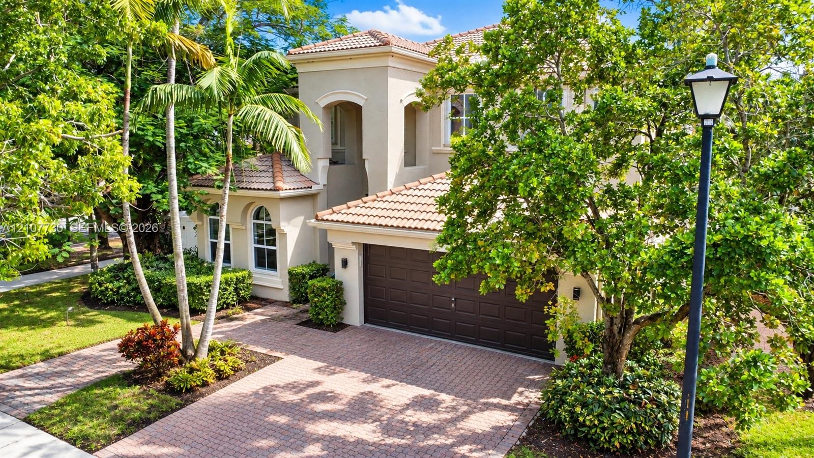 Stucco exterior featuring arched windows, a multi-paneled garage door, a tile roof, and a paved stone driveway