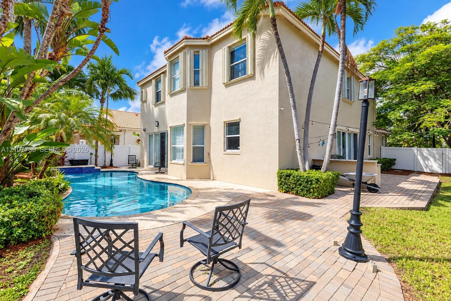 Stucco exterior featuring a two-story bay window, paved patio, in-ground swimming pool, and mature palm trees